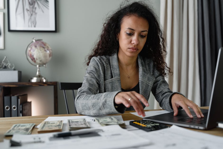 Student reviewing a budget sheet on a laptop at a table with documents
