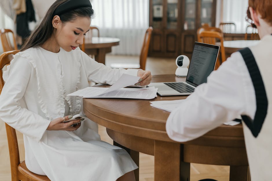 Person uploading application documents to a laptop portal with a checklist nearby
