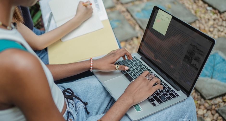 Student at a desk writing steps for a research plan with notes and laptop